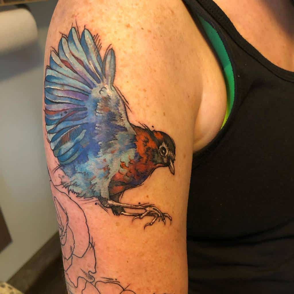 Colorful tattoo of a flying robin with detailed blue and red feathers, blending realism with artistic watercolor effects