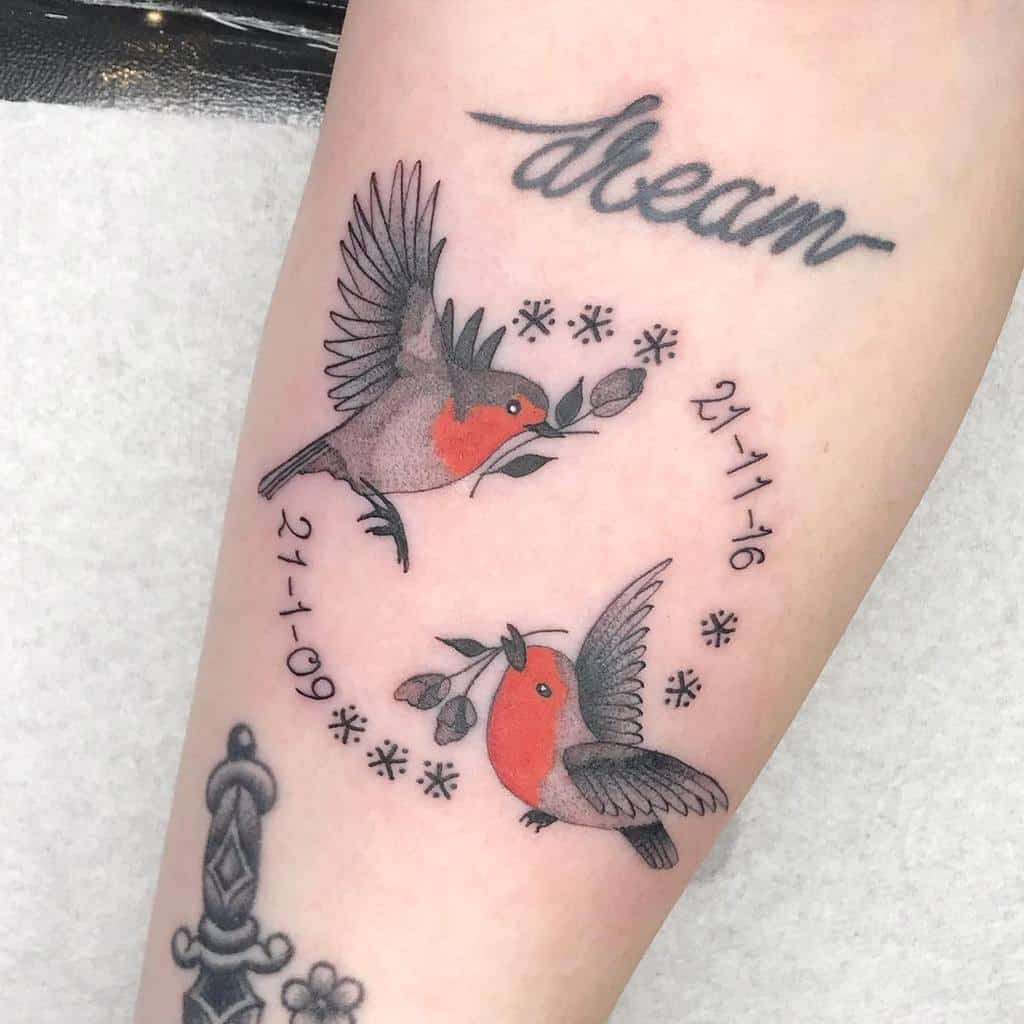 Tattoo of two red-breasted robin holding a rose with leaves, surrounded by dates "21-11-16" and "21-1-09", and snowflakes in circle, with the word "dream" above