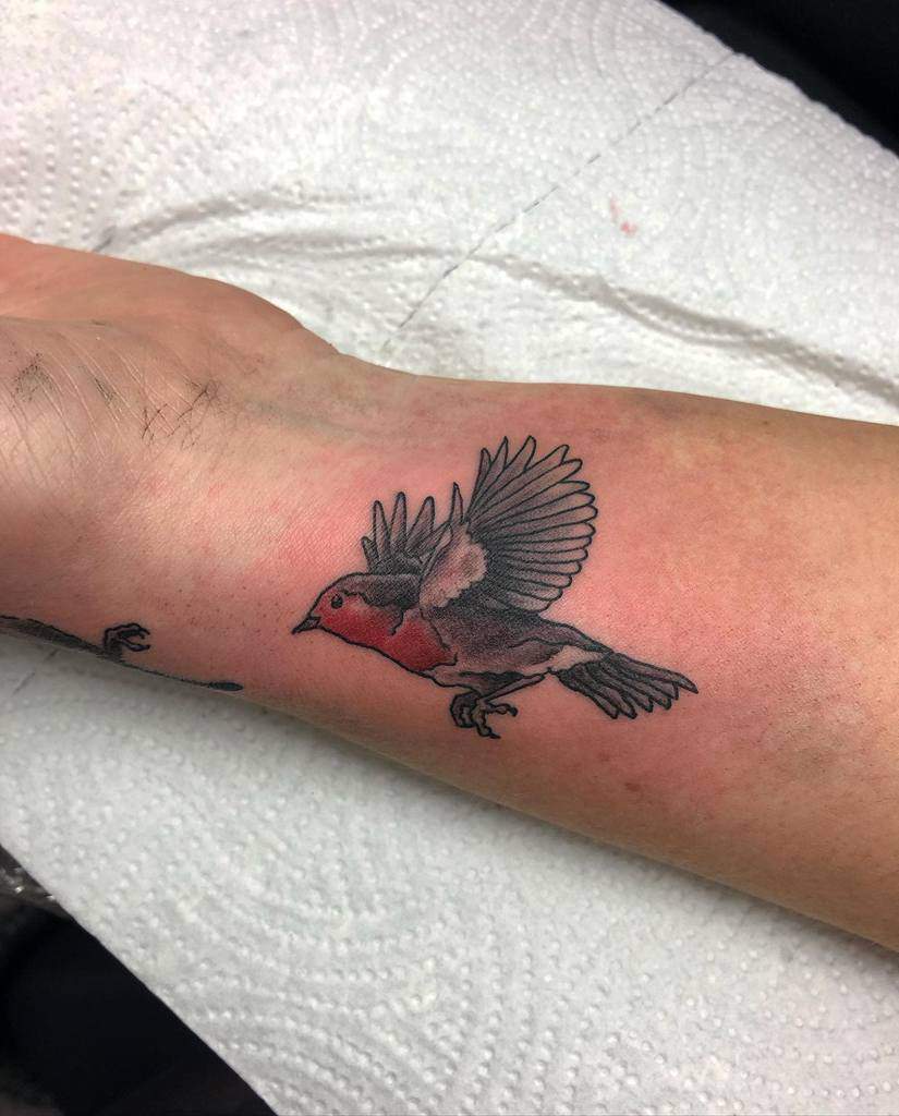 Small tattoo of a robin in mid-flight, with detailed black and grey shading on the wings and a vibrant red chest