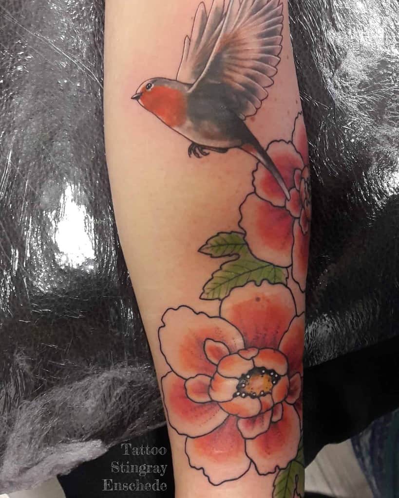 Colorful tattoo of a robin in flight above large orange flowers with green leaves, featuring soft shading and a naturalistic color palette