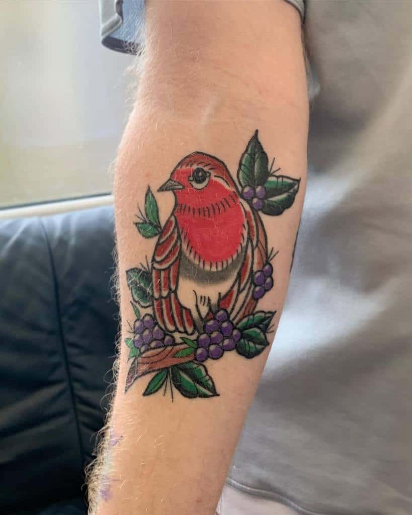 Colorful tattoo of a red and brown robin perched on a branch with green leaves and purple berries