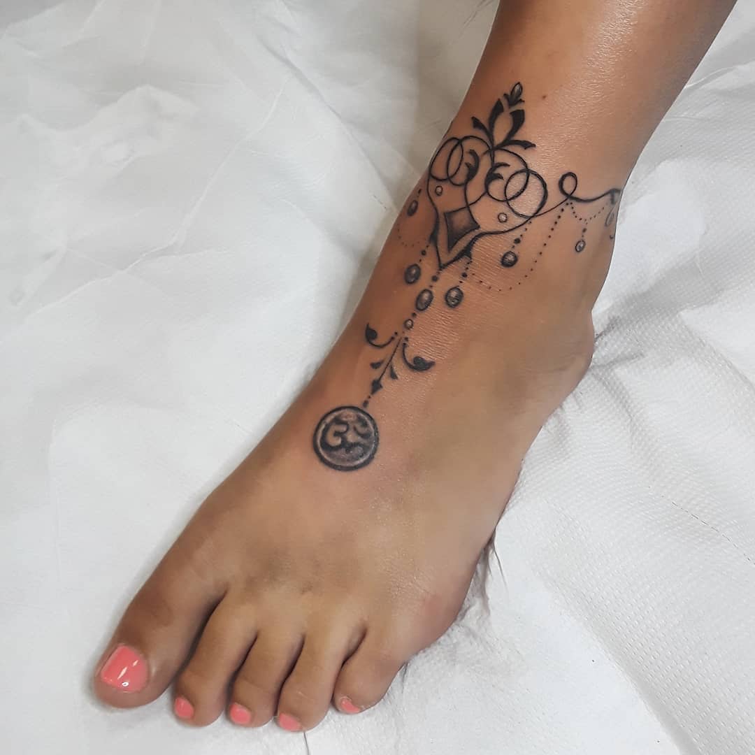 A foot with a delicate, circular floral and ornamental black tattoo across the top and side of the ankle
