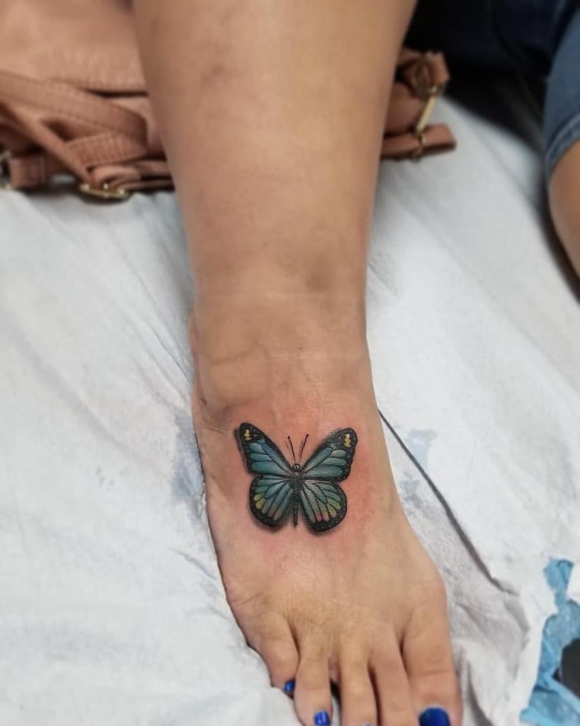 A vibrant blue butterfly tattoo adorns the top of a person's foot