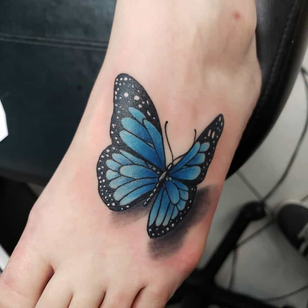 Blue butterfly tattoo on a person's foot, showcasing intricate black and white accents