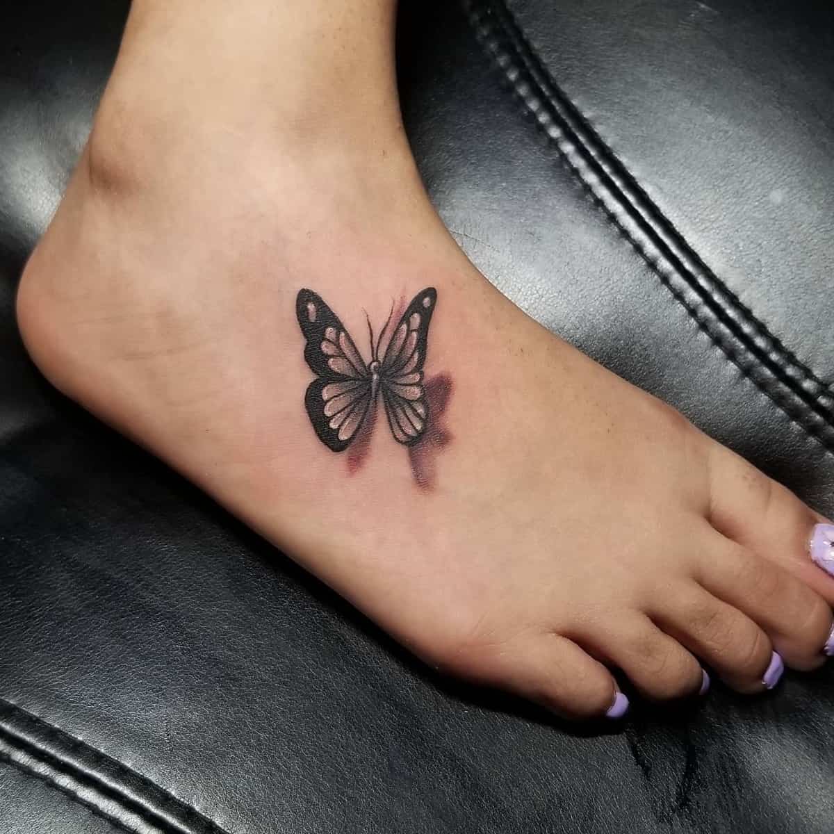 A foot with a black and shaded butterfly tattoo on the top, toes painted in light violet nail polish