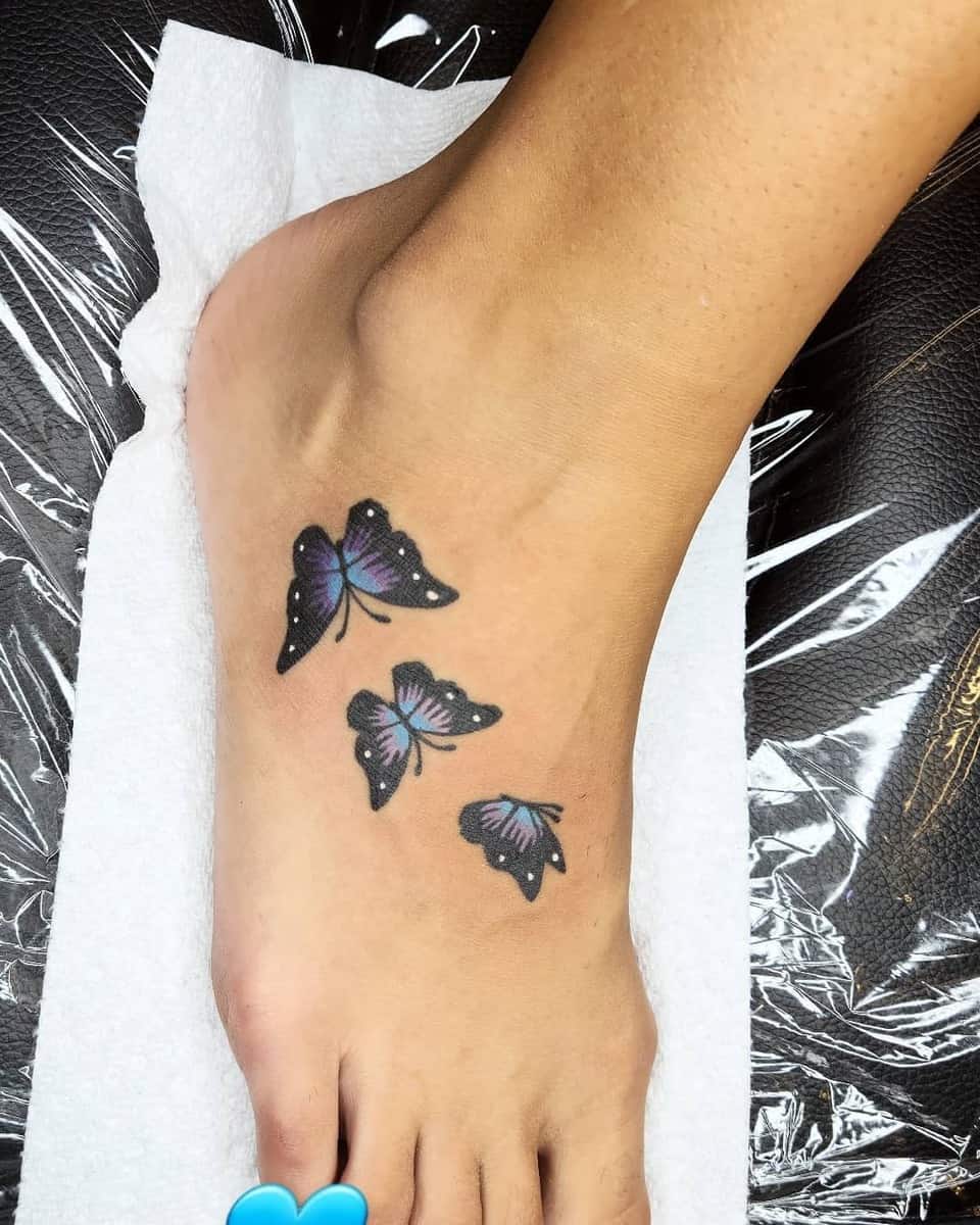 A foot tattoo of three black and purple butterflies on the top of a foot