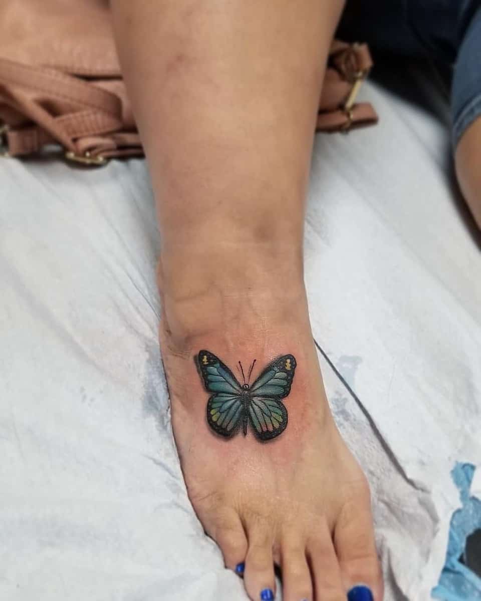 A colorful butterfly tattoo on the top of a foot