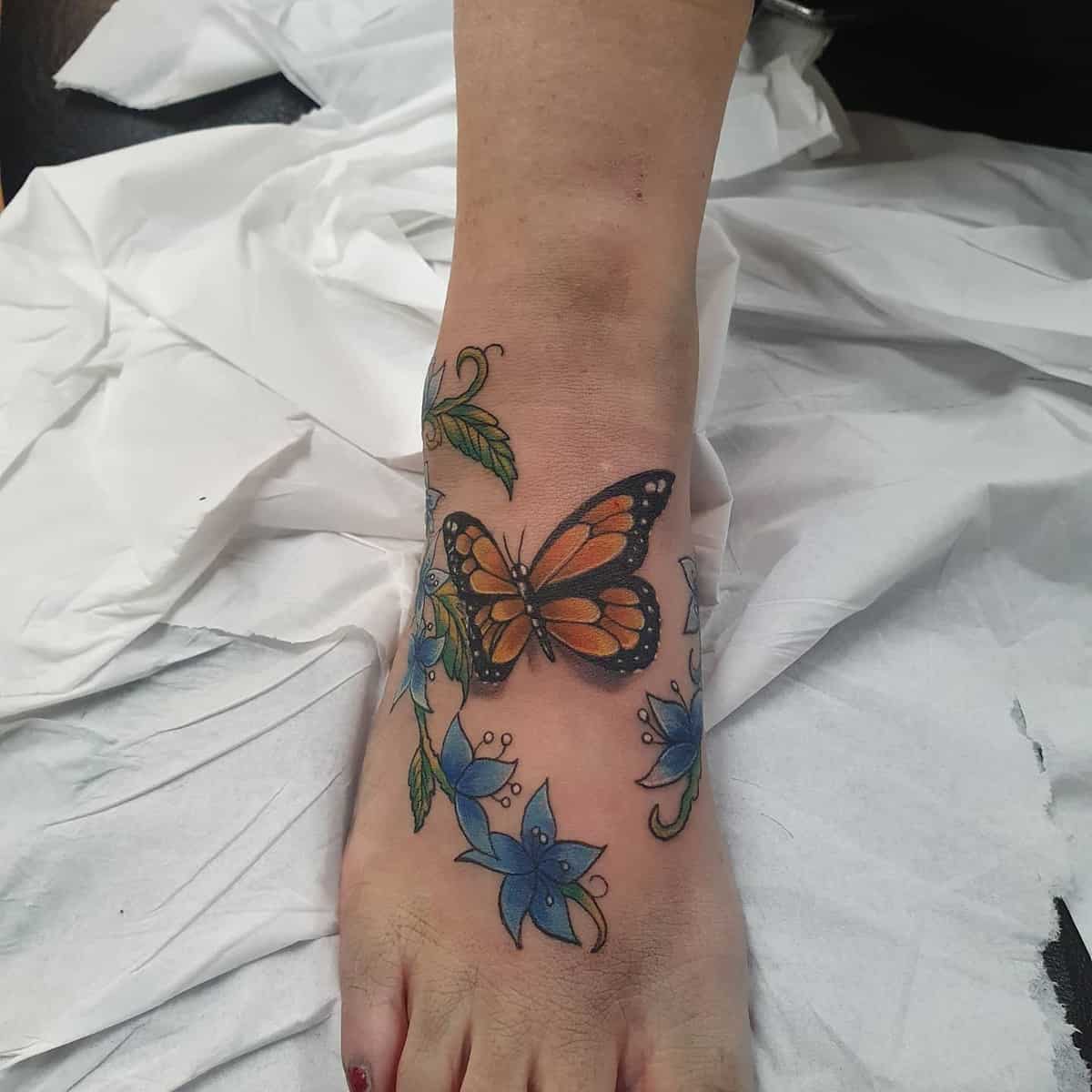 A foot with a tattoo featuring a butterfly and blue flowers on the top