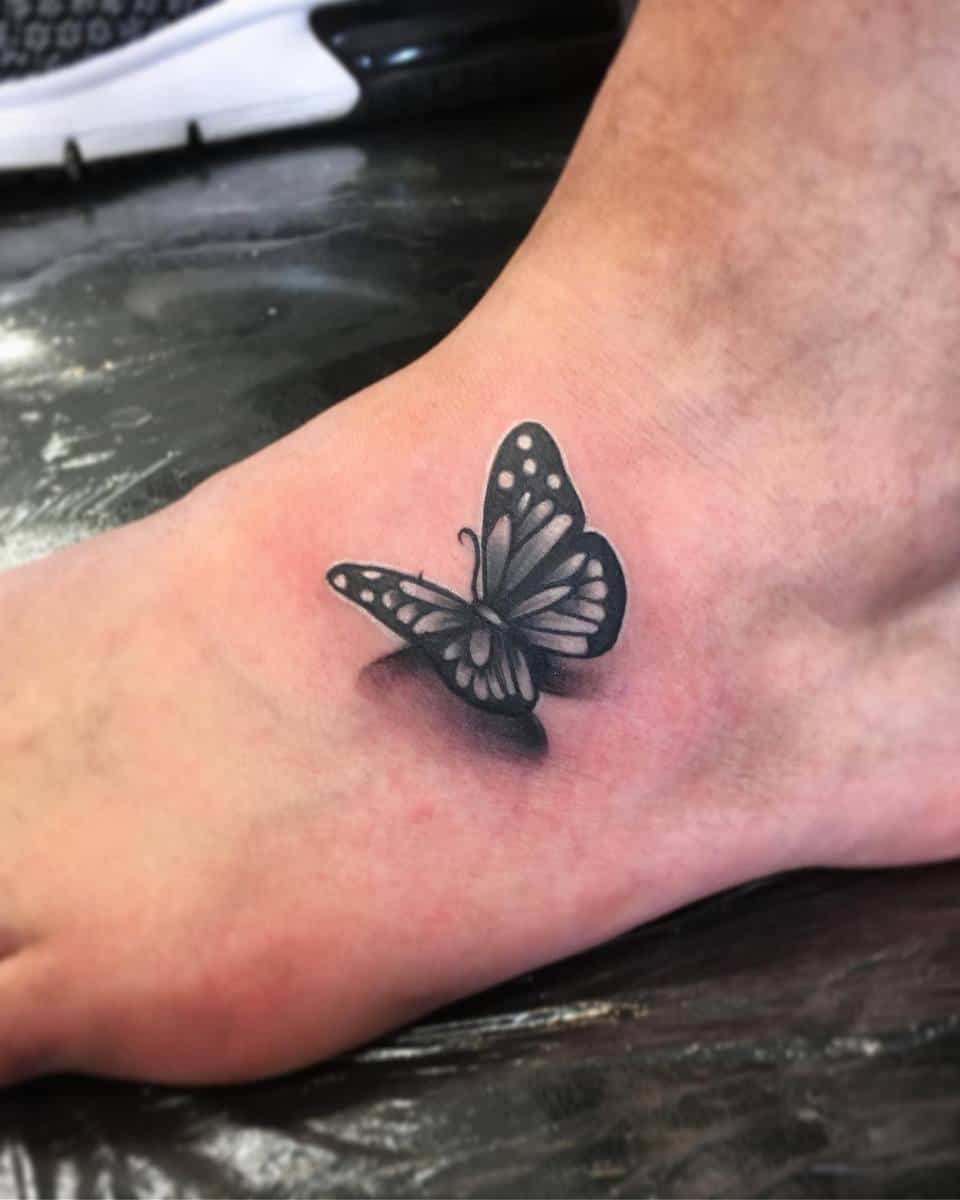 A black-and-white butterfly tattoo on the top of a foot