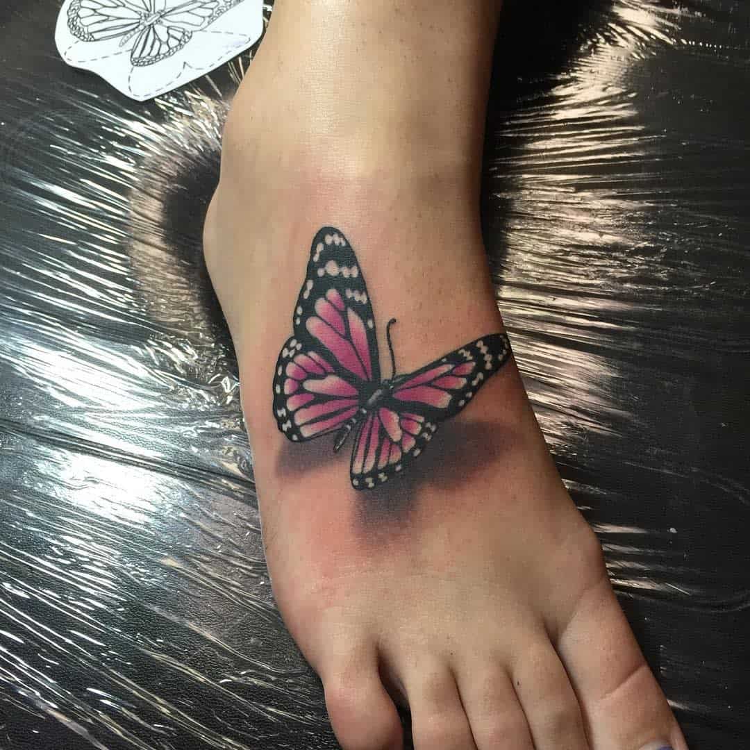 A vibrant pink and black butterfly tattoo on a foot with a paper butterfly design beside it
