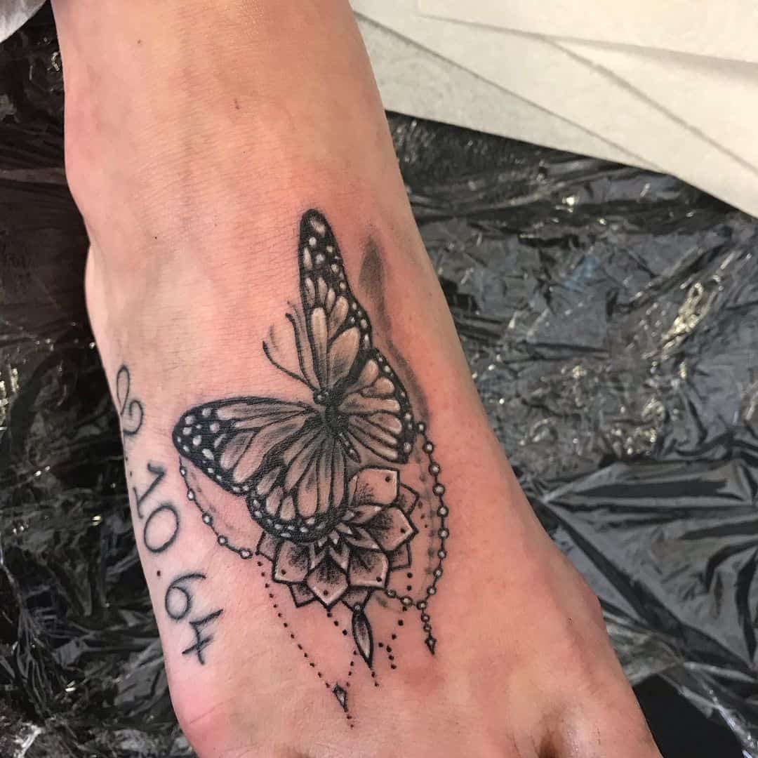 Black and white butterfly tattoo on a foot with the date 29.10.64 and decorative elements