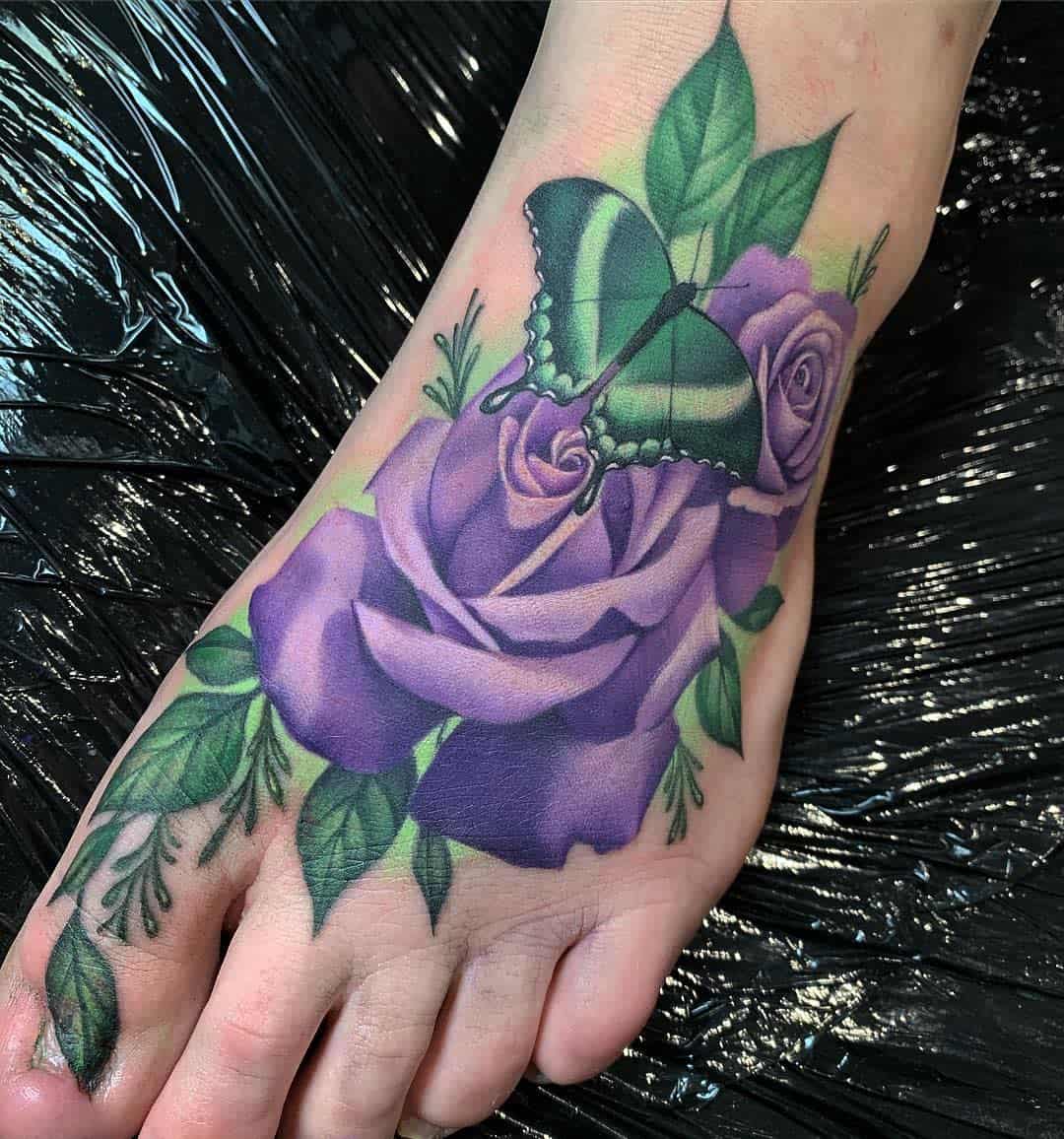 A foot tattoo featuring a green butterfly resting on vibrant purple roses with green leaves