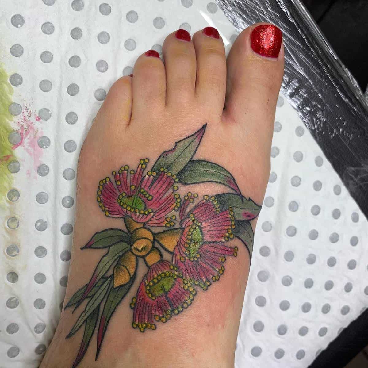 A foot with a colorful tattoo of pink flowers and green leaves, and red painted toenails