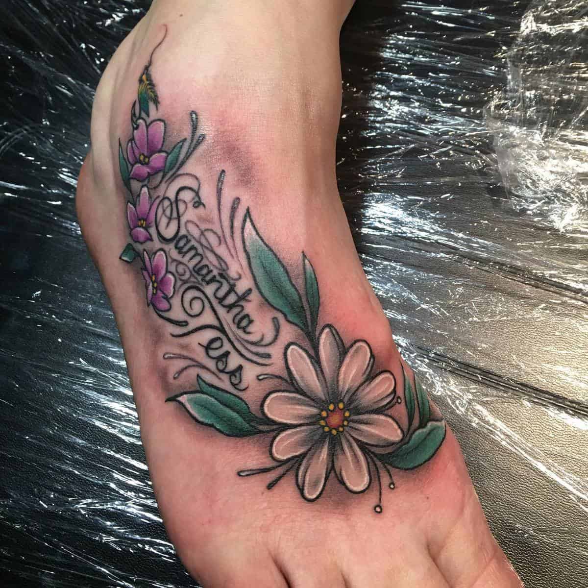 Foot tattoo featuring pink and white flowers, green leaves, and cursive names "Samantha" and "Tess