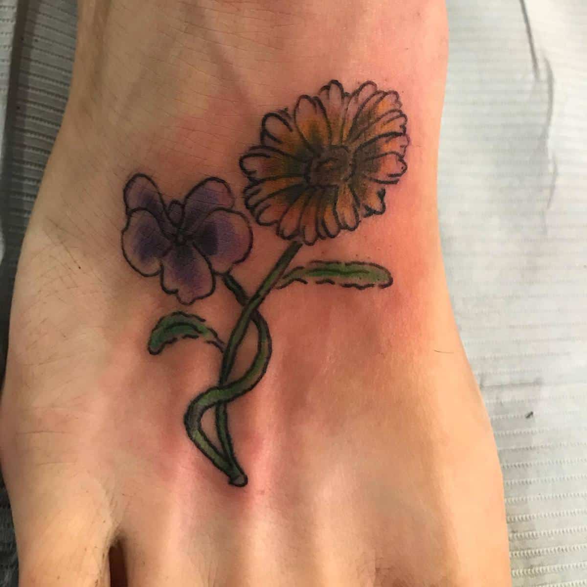 Foot tattoo of a purple and yellow flower with green stems and leaves on slightly red, irritated skin