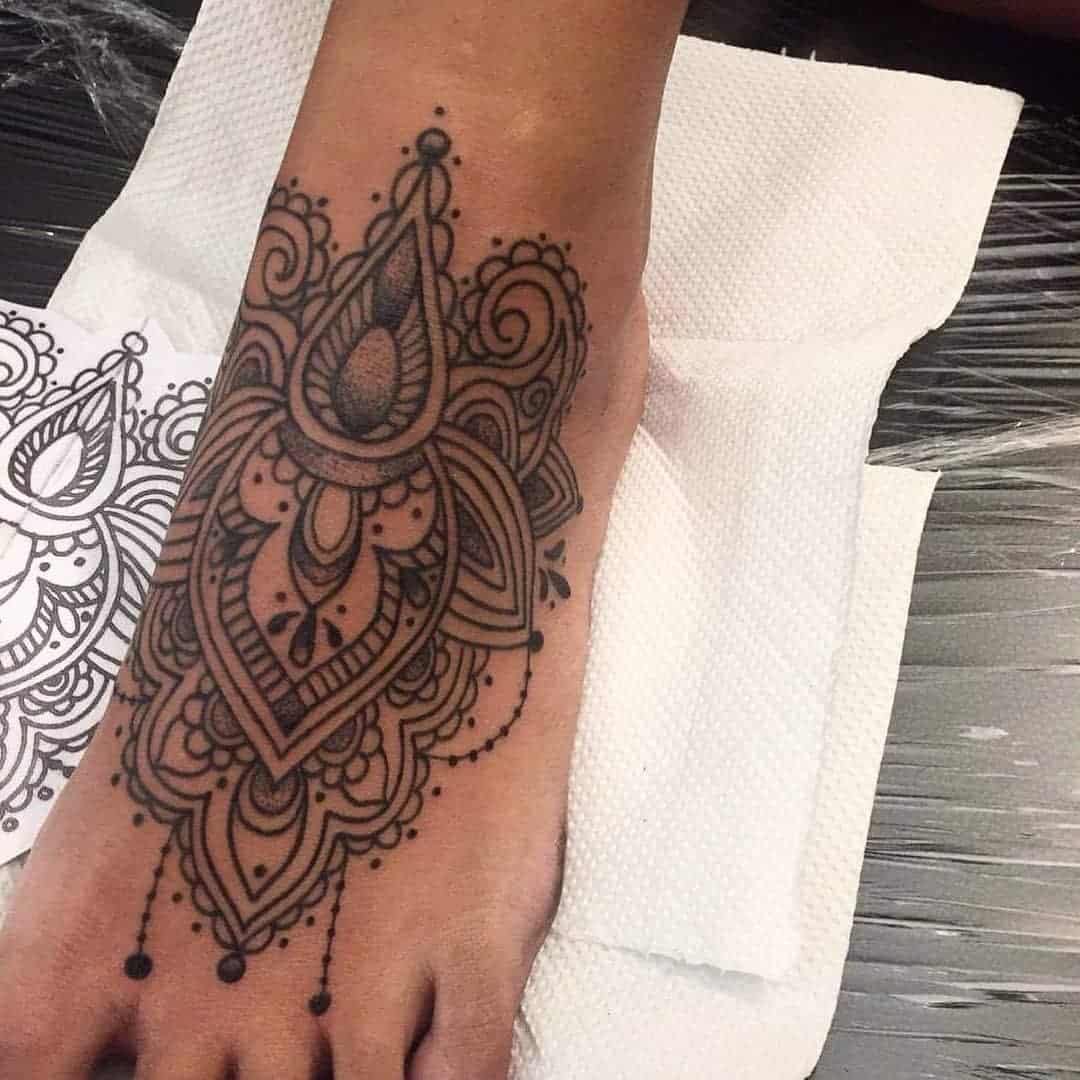 A detailed, ornate mandala tattoo design on top of a foot, featuring intricate patterns and dot work