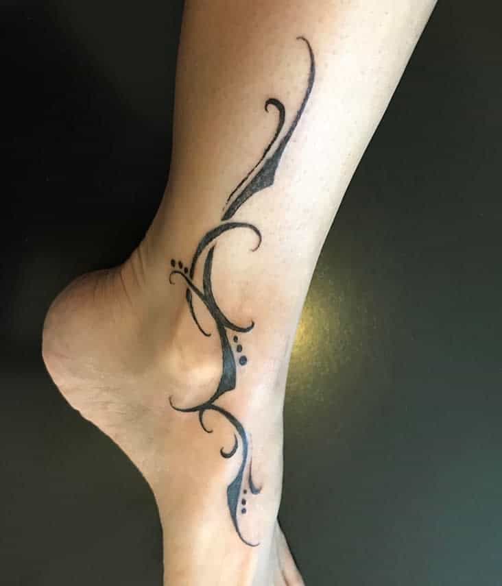 A leg features a black abstract tattoo design flowing from the mid-calf to the foot