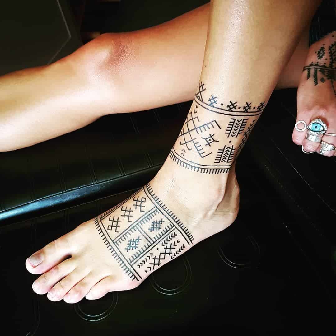 Ankle and foot with intricate tribal tattoos, toes adorned with rings featuring turquoise stones