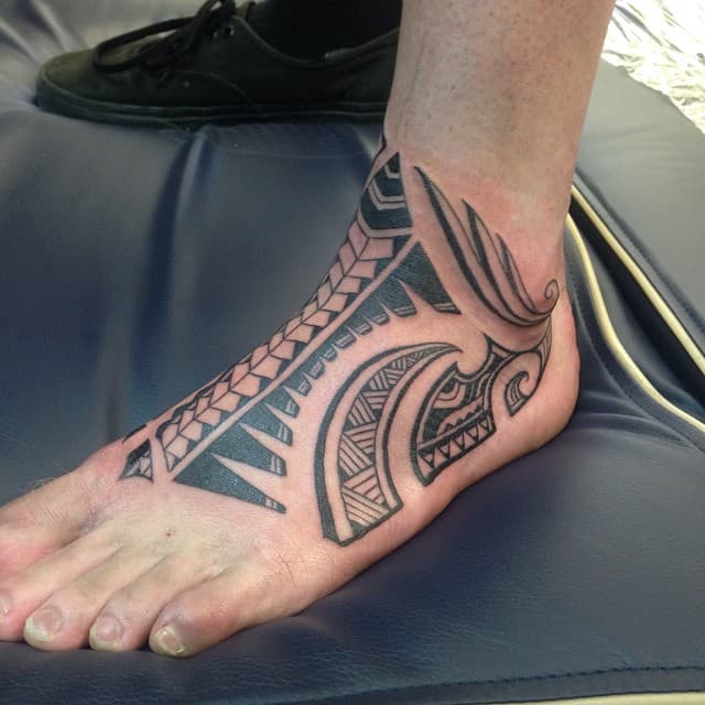 A foot adorned with a detailed tribal-style tattoo featuring bold black geometric and curved patterns