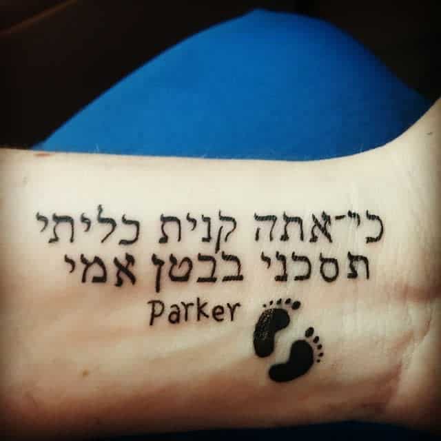 Tattoo on arm with Hebrew text, small footprints, and the word "Parker"