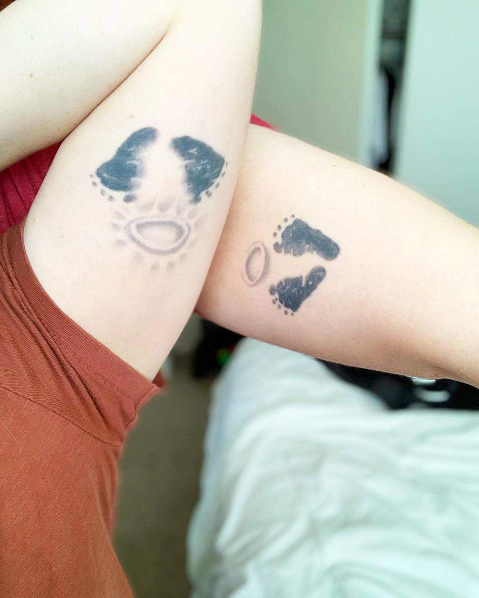 Two arms with matching tattoos of baby footprints and ellipses