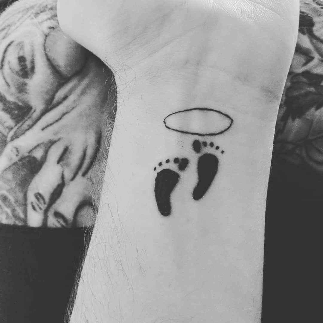Black and white tattoo of small footprints and a halo on a wrist