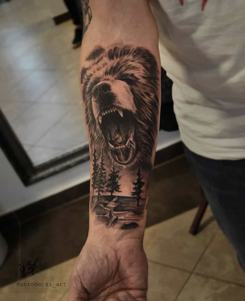 Forearm tattoo of a fierce, roaring bear with a lush forest scene in the background