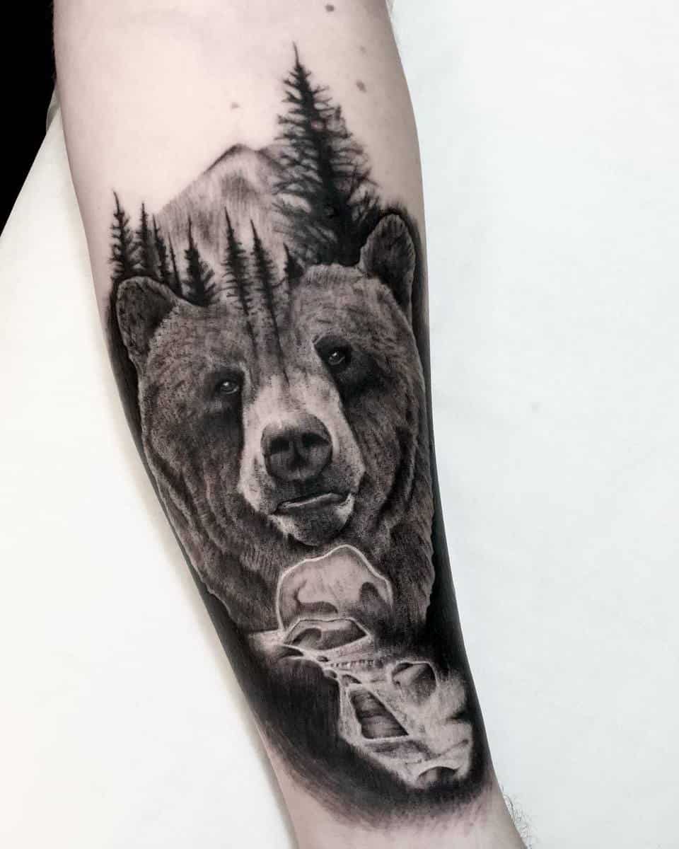 Arm tattoo featuring a bear in a forest with mountains in the background