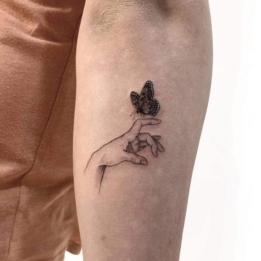 Tattoo of a hand with a butterfly on the forearm