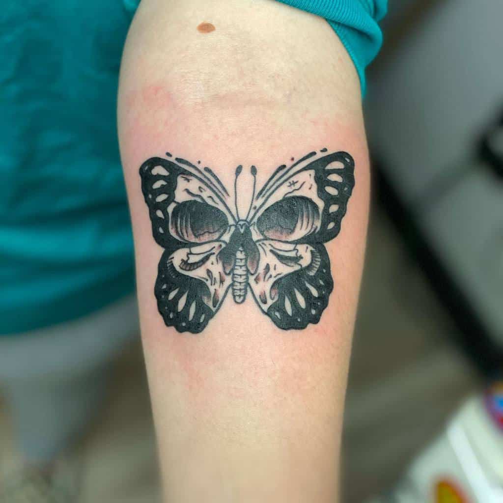 A black and white butterfly tattoo is inked on a person's forearm with a human skull in its wings