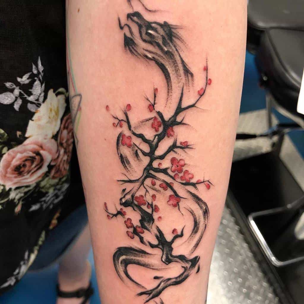 A cherry blossom tree tattoo with black ink and red flowers on a woman's arm