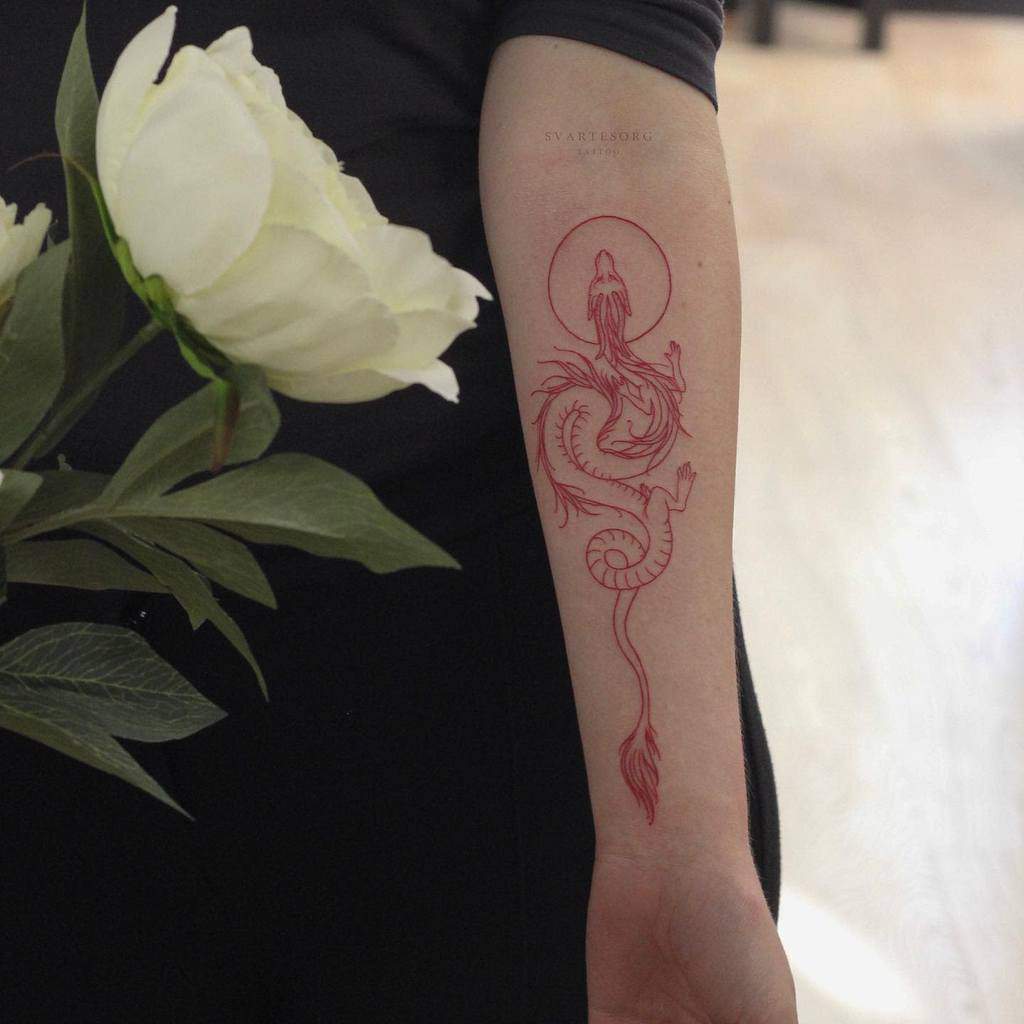 Red dragon tattoo on forearm next to a white rose