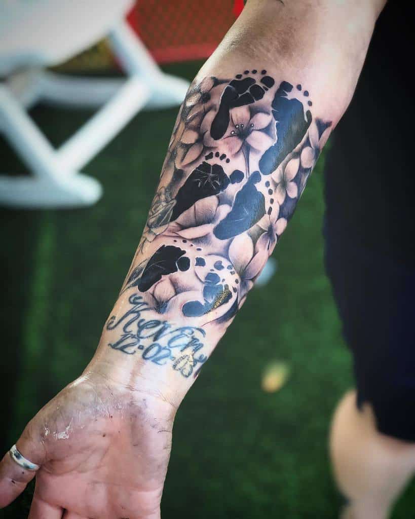 A stunning forearm tattoo sleeve showcases baby footprints and decorative script, weaving a timeless story on the skin