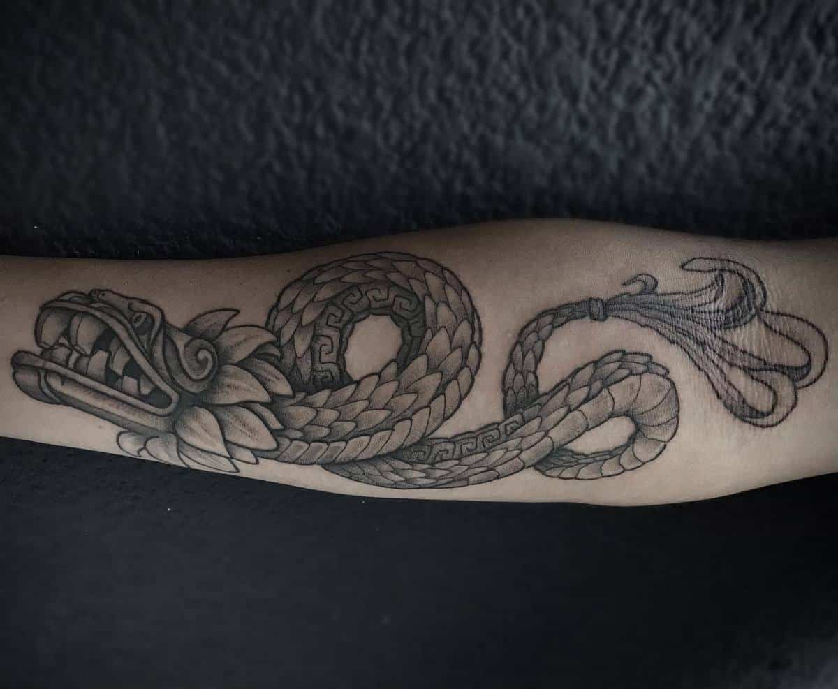 Black and gray Quetzalcoatl forearm tattoo featuring a coiled serpent with intricate details