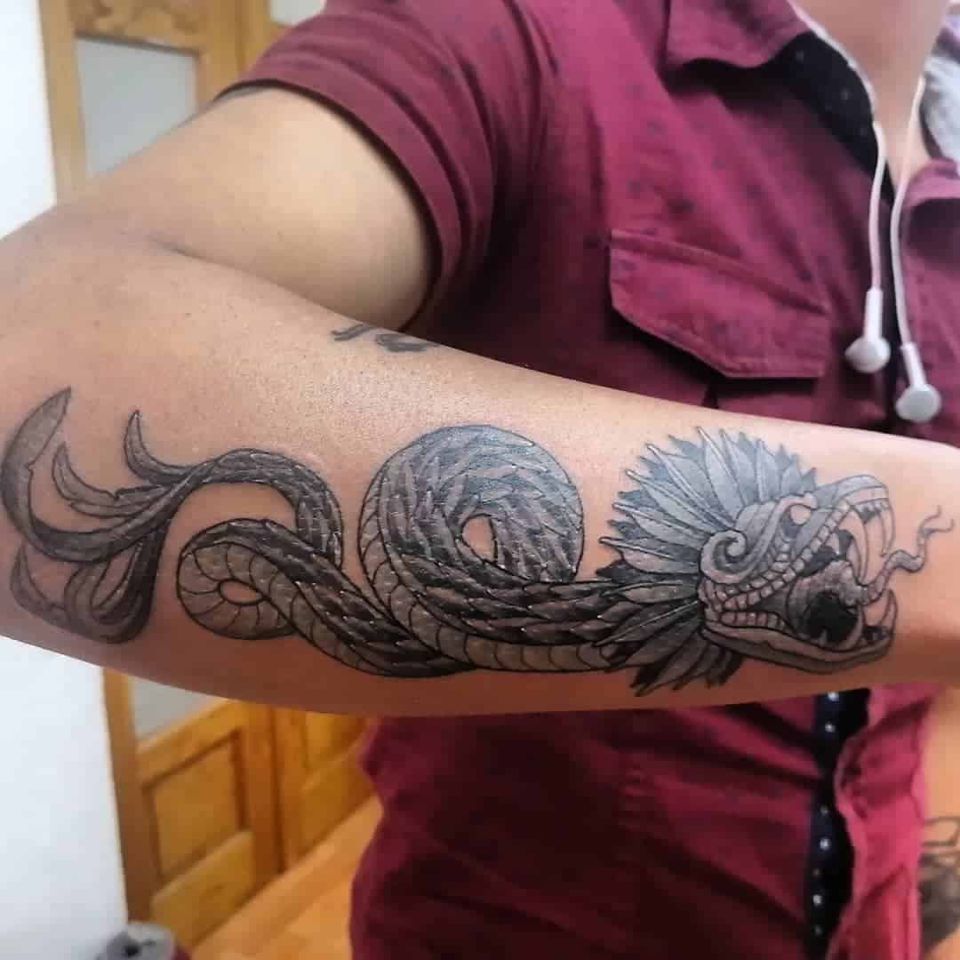 Detailed Quetzalcoatl forearm tattoo with a feathered serpent design wrapping around the arm