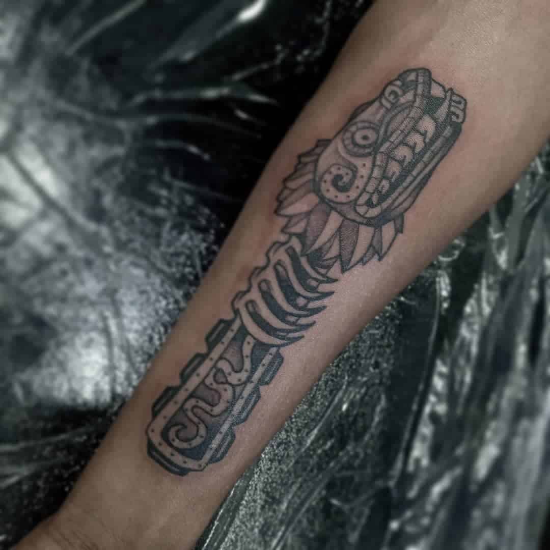 Black and gray Quetzalcoatl forearm tattoo featuring a stylized serpent head and skeletal body