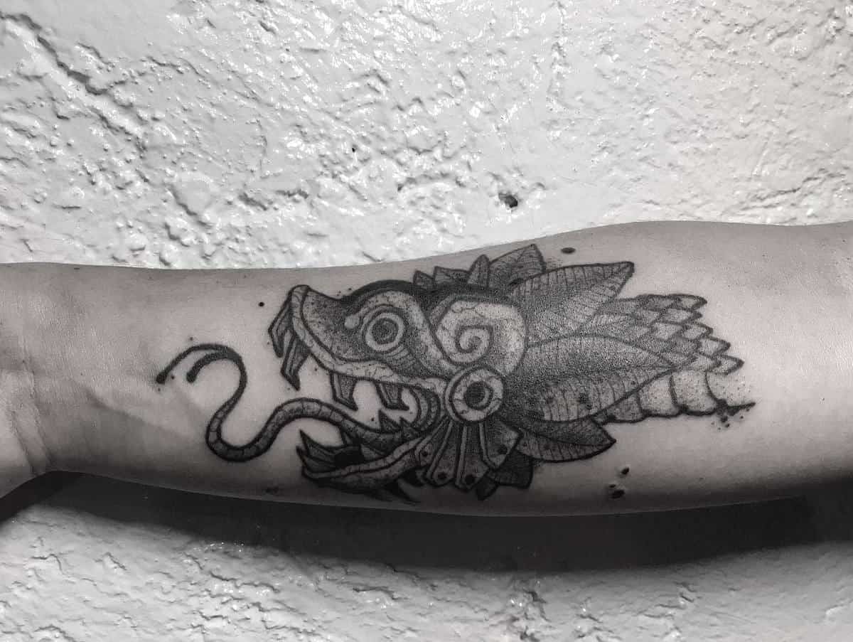 Black and gray Quetzalcoatl forearm tattoo featuring a stylized feathered serpent head with intricate details