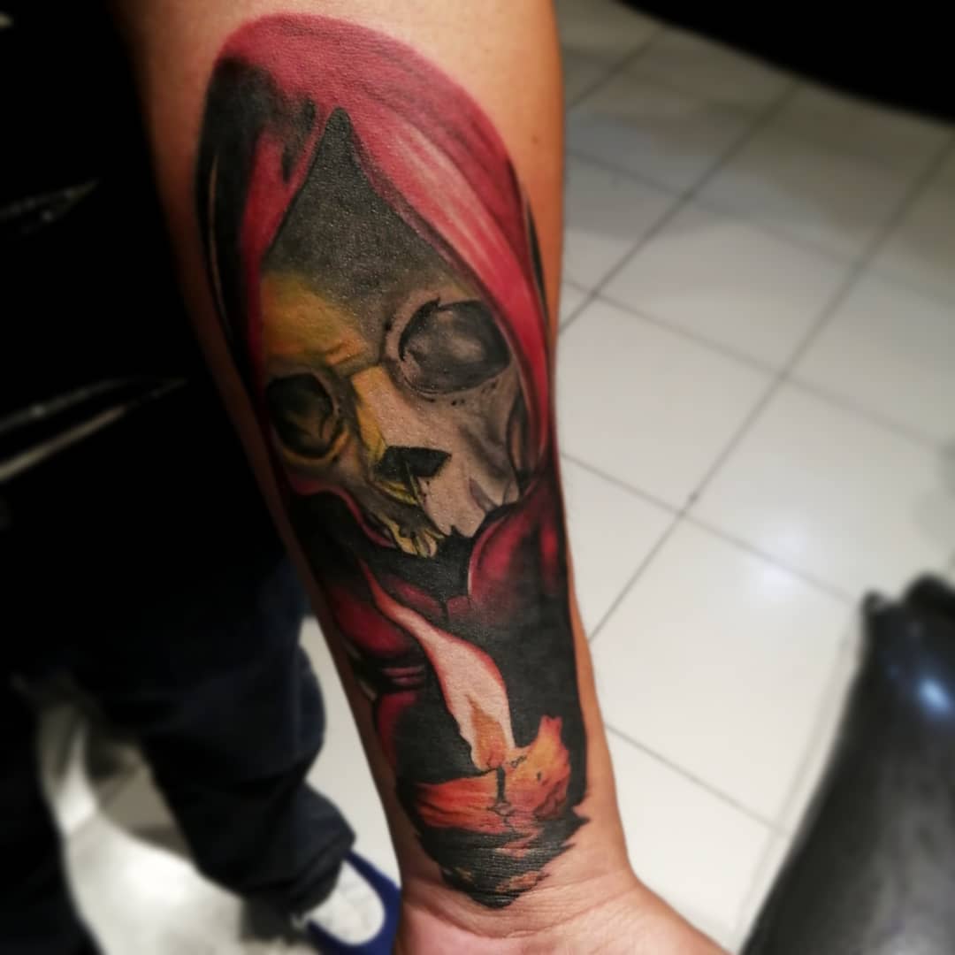 Colorful Santa Muerte tattoo featuring a skeletal figure cloaked in red, holding a glowing candle