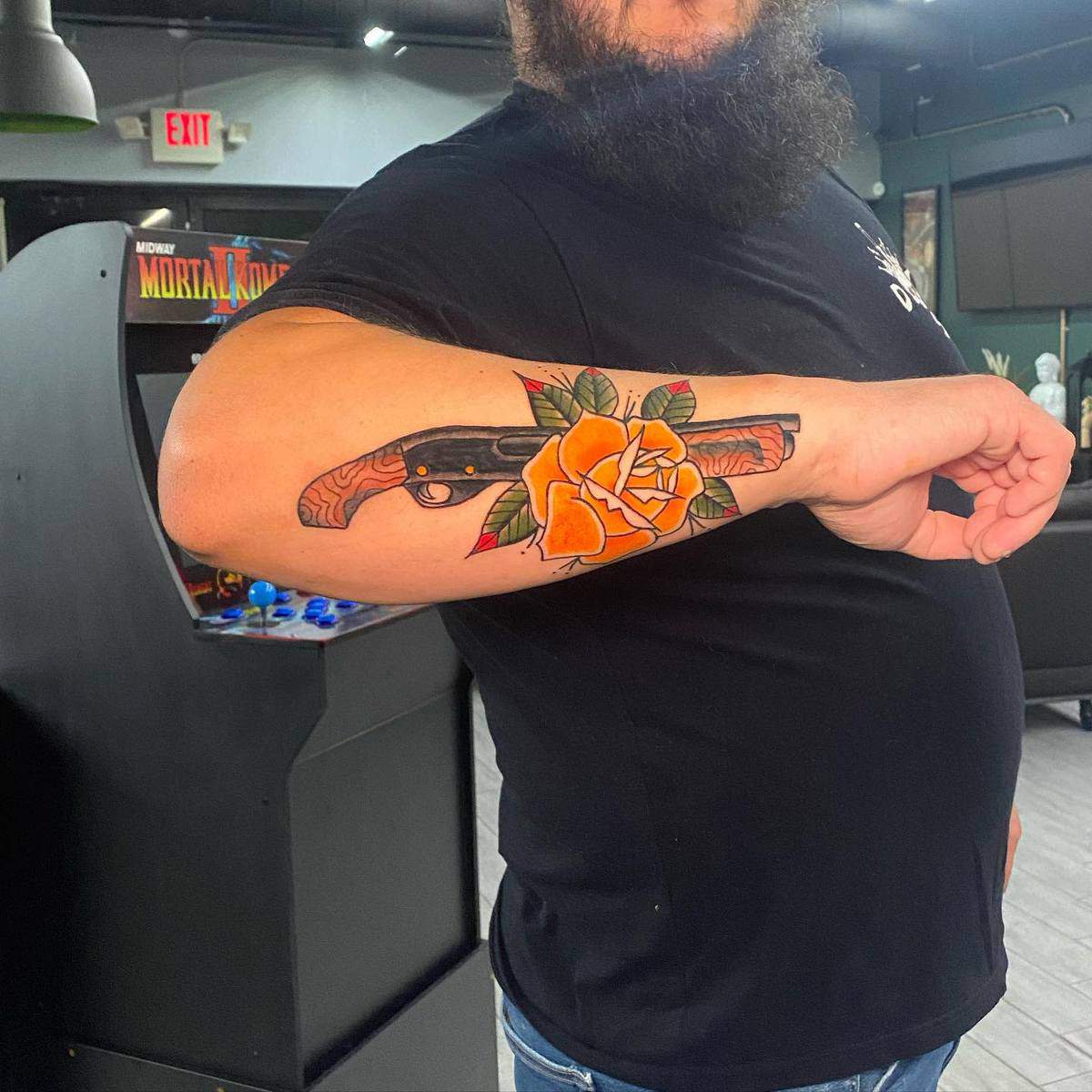 Showing off a tattoo of a shotgun with a yellow rose on their forearm
