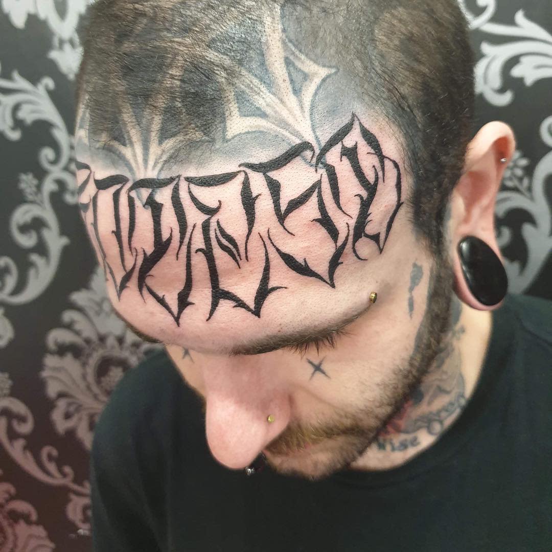 Man with intricate black forehead tattoo and multiple facial piercings