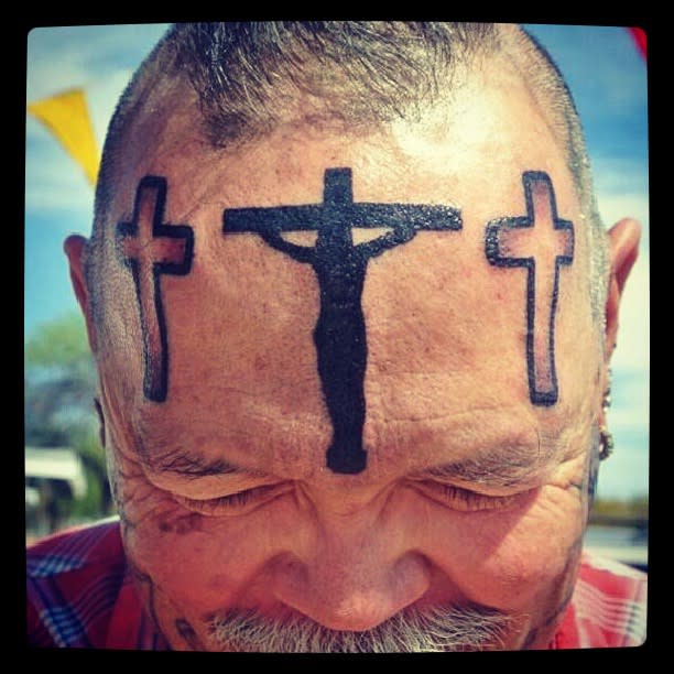 A man with three cross tattoos on his forehead, one in the center featuring a crucifix