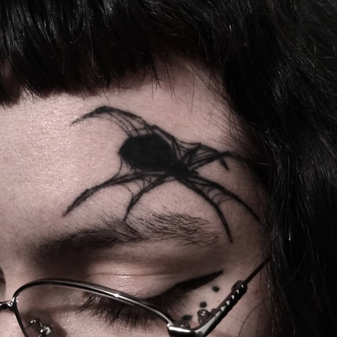 Black spider tattoo on forehead above closed eye