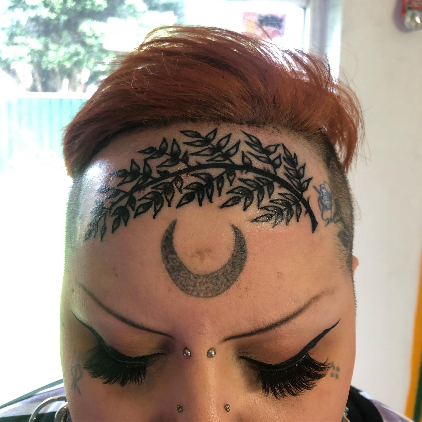 Individual with a crescent moon and leaf tattoos on their forehead