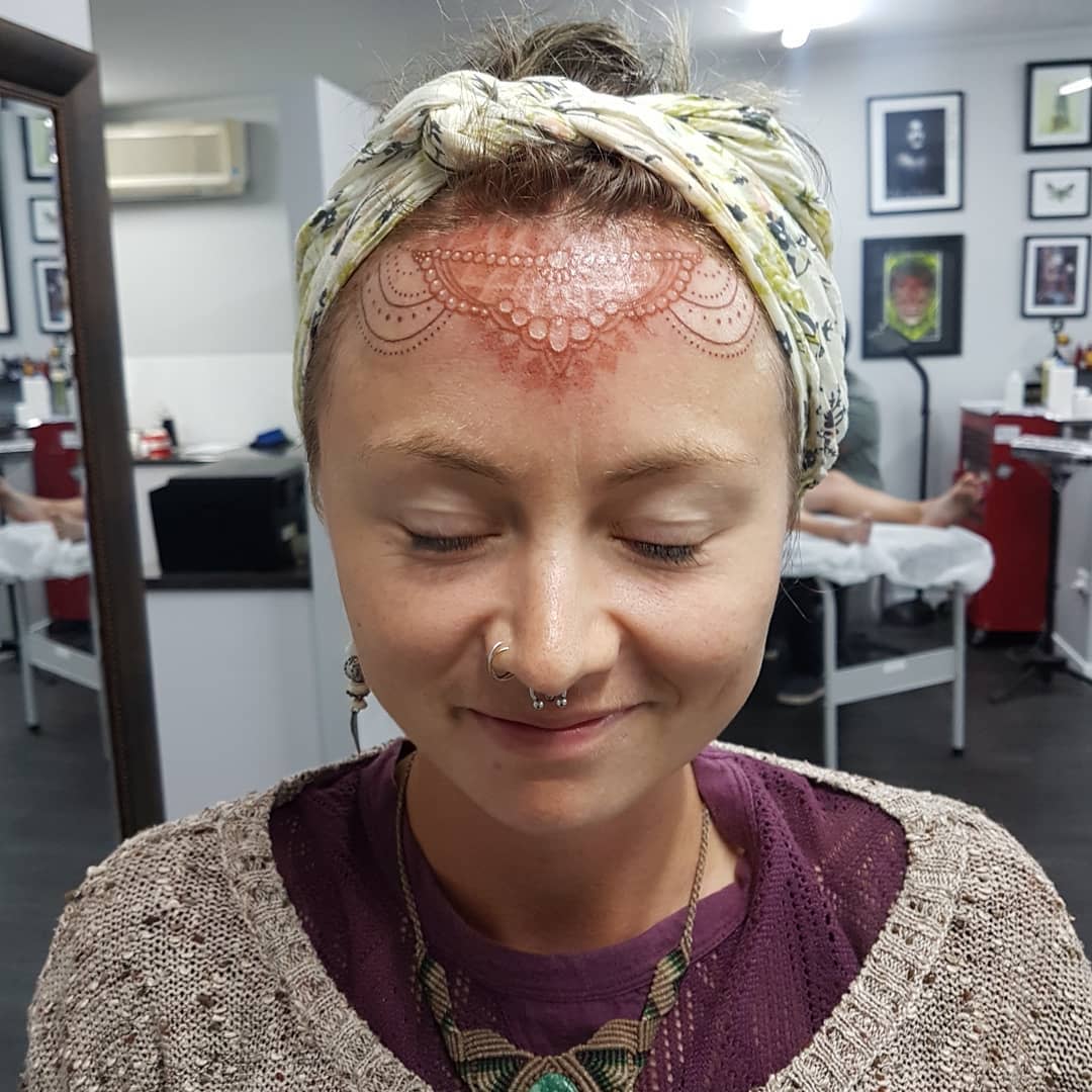 Mandala tattoo on forehead featuring intricate geometric patterns and floral elements