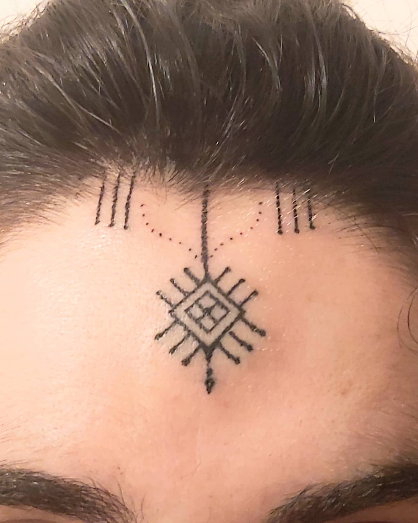 A geometric tattoo design on the forehead near the hairline