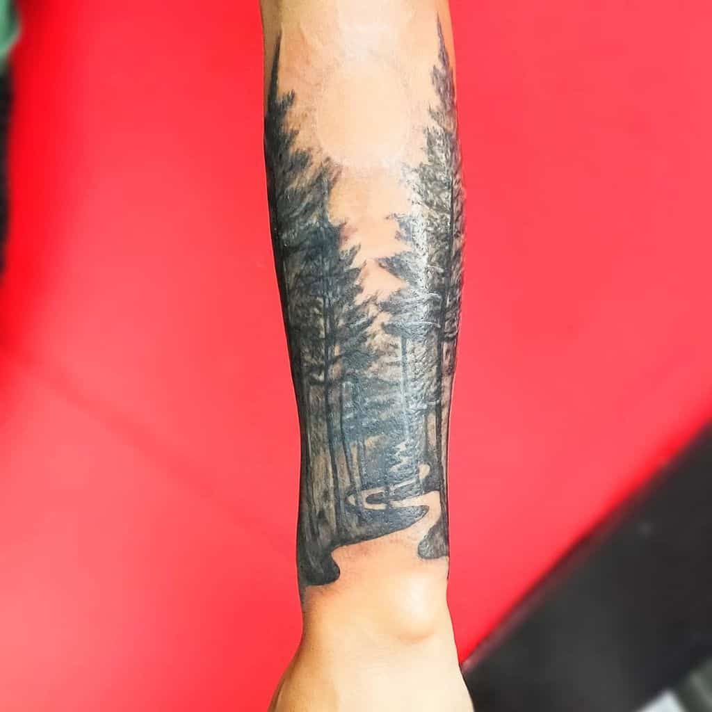 Forearm tattoo of a winding path through a forest of tall evergreen trees