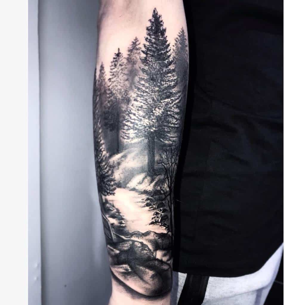 A detailed forest scene tattoo with trees and a river on a person's forearm