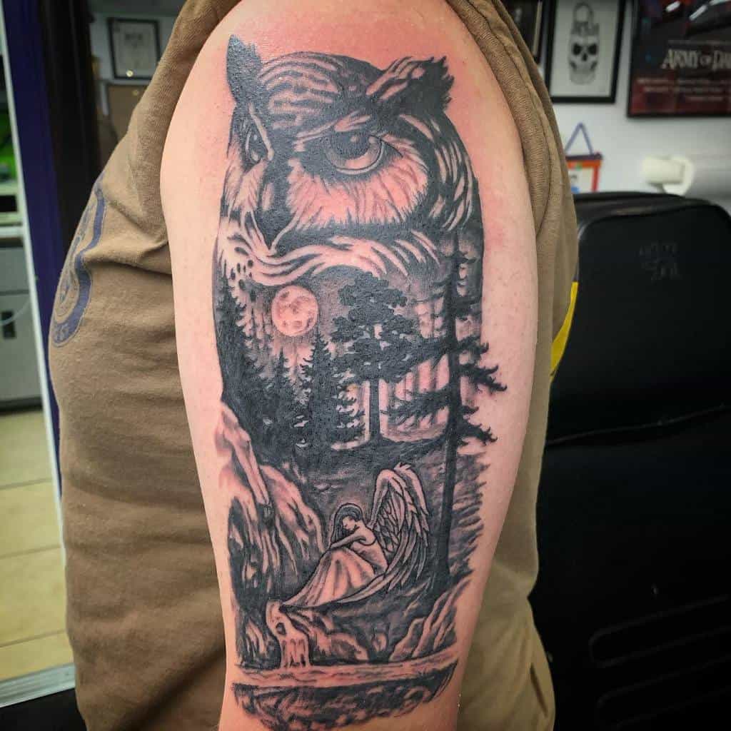 Tattoo of an owl, forest, moon, and angel on a person's upper arm with the silhouette of trees adding depth