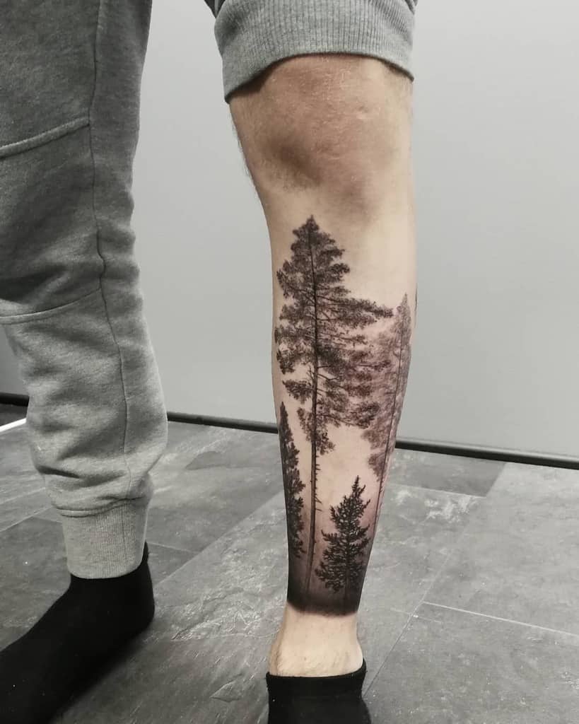 Leg tattoo of a silhouette of tall pine trees in a forest