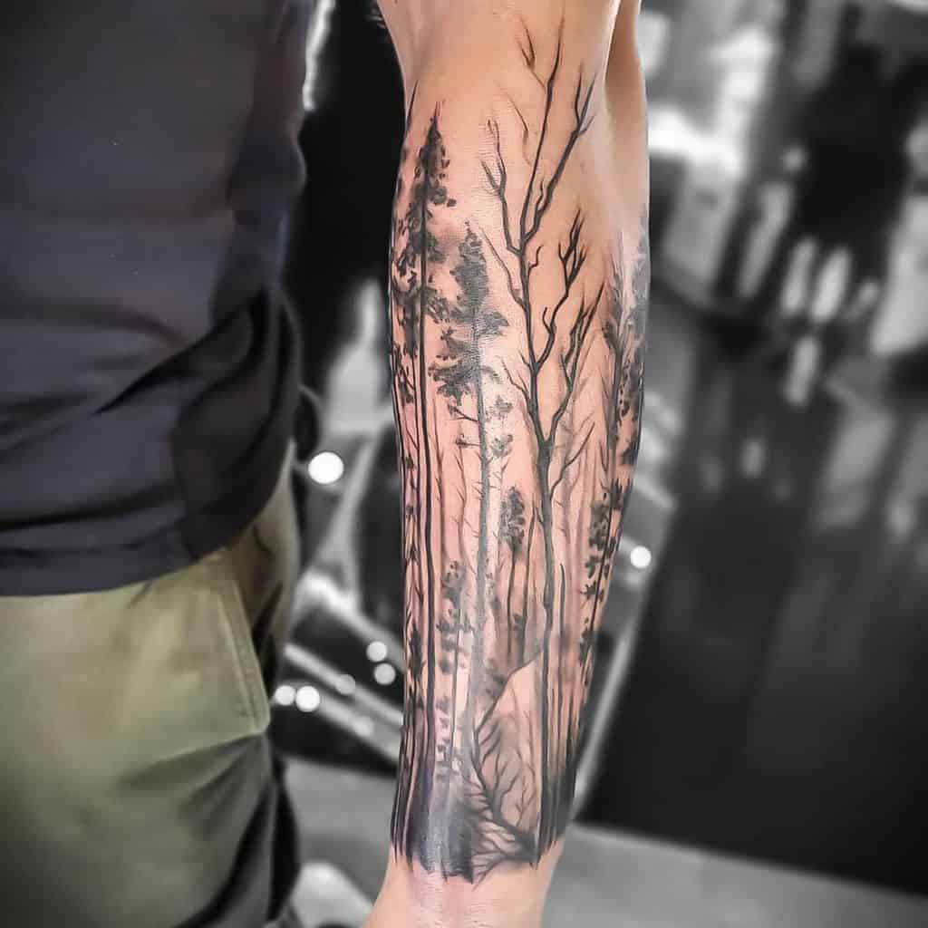 Forearm tattoo featuring intricate trees and forest scenery in black and grey ink